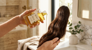 A professional editorial close-up of a high-quality glass bottle of golden hair oil being drizzled n